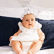 Amalia a rejoint le concours — aidez-le/la à gagner de superbes lots ! baby, bed, blue_pillow, child, chubby_legs, curious_expression, cute, face, flower_crown, hands, headband, indoors, infant, legs, portrait, sitting, skin, soft_lighting, white_bed_sheet, white_dress