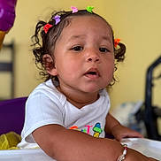 Kyelynn joined the competition — help win amazing prizes! toddler, child, hair_clips, bracelet, white_shirt, table, curly_hair, indoor, expression, face, portrait, person, sitting, colorful, closeup, young_child, beaded_bracelet, casual_clothing, background_blur, skin