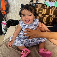 Emna participe au concours pour gagner de l'argent avec cette photo : baby, child, smiling, dress, pink_shoes, curly_hair, pigtails, hand_support, blanket, indoor, dresser, clutter, backpack, person, happy, cute, infant, seated, home, portrait