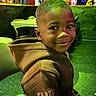 child, young_boy, smiling, portrait, indoor, restaurant, entertainment_venue, neon_lighting, colorful_lights, hoodie, brown_clothing, elite_text, seated, table, chair, bar_area, green_lighting, nightlife, candid_photo, happy