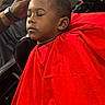 child, boy, sleeping, barbershop, haircut, red_cape, portrait, face, short_hair, adult_hand, barber, grooming, chair, indoor, closeup, black_clothing, watch, relaxed, haircutting, photograph