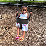 De Onni joined the competition — help win amazing prizes! toddler, child, smiling, swing, playground, outdoor, park, tennis_court, sports_facility, wood_chips, dress, sandals, hair_bows, portrait, happy, sitting, play_equipment, tree, chain, daylight