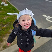 Mattias a rejoint le concours — aidez-le/la à gagner de superbes lots ! backpack, blonde_hair, casual_clothing, child, coat, cute, grass, handicapped_sign, happy, hat, joyful, outdoor, parking_lot, person, playful, red_pants, shoes, sidewalk, smiling, toddler