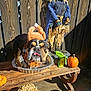 bulldog, dog, costume, turkey_hat, pumpkin, plush_toy, football_toy, scarecrow, wooden_bench, hay, outdoor, sunlight, fall_decor, tongue_out, pet, animal, festive, celebration, funny, background
