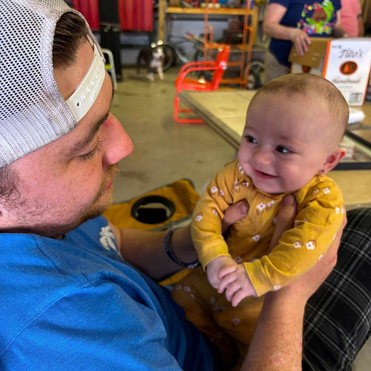 Sylvie joined the competition — help win amazing prizes! baby, background, blue_shirt, cap, casual, chair, face, family, hands, happy, holding, indoor, interaction, man, people, plaid_pants, portrait, smile, table, yellow_clothing