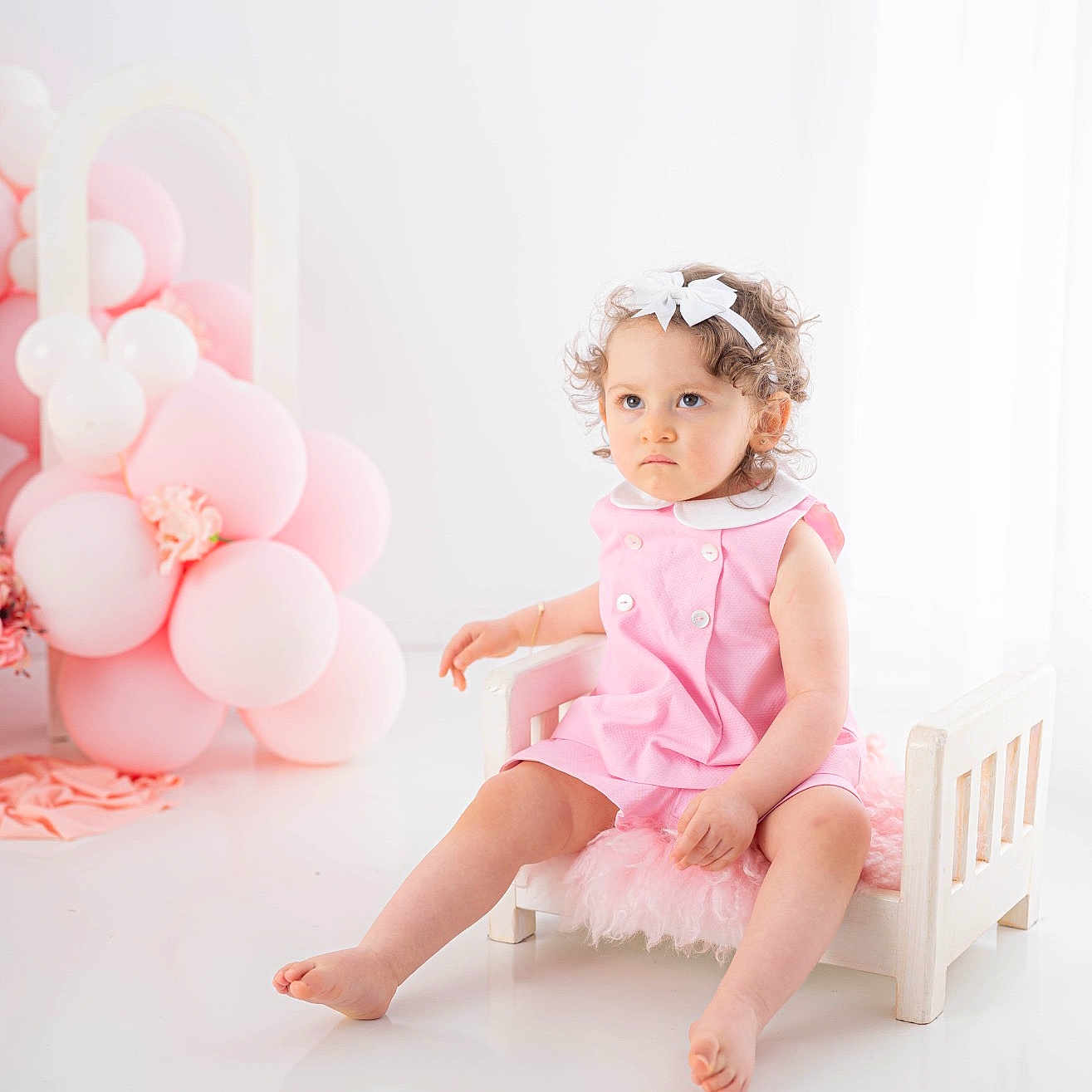 Elyana a rejoint le concours — aidez-le/la à gagner de superbes lots ! toddler, child, pink_dress, white_bow, curly_hair, balloons, pink_balloons, white_balloons, small_chair, wooden_chair, fluffy_cushion, indoor, studio, portrait, serious_expression, barefoot, floor, decor, cute, baby