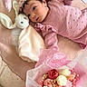 baby, infant, pink_clothing, headband, plush_toy, bunny, blanket, flower_bouquet, flowers, soft_texture, lying_down, cute, child, portrait, indoor, pastel_colors, decor, hand, face, young_child