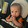 Jacob is registered to the contest to win money with this photo: baby, infant, car_seat, blanket, orange_shirt, child, seatbelt, hands, face, wide_eyes, expression, indoor, safety_warning, headrest, cute, young_child, car_interior, serious, wrapping, seat