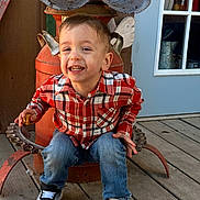 Maverick is registered to the contest to win money with this photo: child, toddler, boy, smiling, portrait, outdoor, seated, chair, antique, metal, plaid_shirt, jeans, sneakers, snack, backyard, wooden_floor, door, window, happy, face
