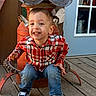 child, toddler, boy, smiling, portrait, outdoor, seated, chair, antique, metal, plaid_shirt, jeans, sneakers, snack, backyard, wooden_floor, door, window, happy, face