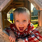 Levi is registered to the contest to win money with this photo: child, toddler, boy, smiling, laughing, portrait, face, blond_hair, plaid_shirt, red_shirt, wooden_playhouse, window, outdoor, sunlight, rustic, playground, happy, sitting, hands, candid