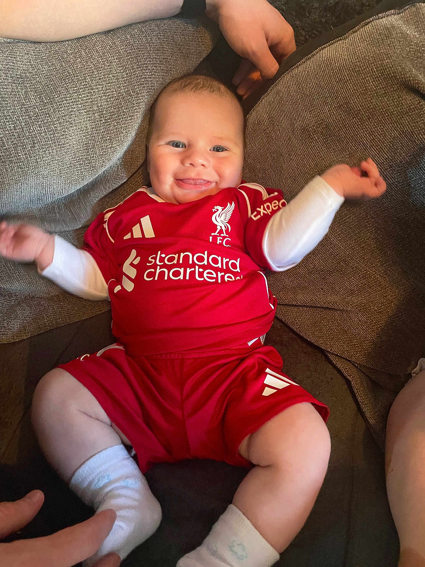 Mercier is registered to the contest to win money with this photo: baby, infant, smiling, red_clothing, football_kit, socks, couch, person, happy, cheerful, indoor, hand, sportswear, seated, cute, child, furniture, relaxed, tongue_out, support