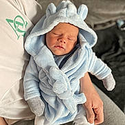 Mercier is registered to the contest to win money with this photo: baby, newborn, sleeping, hooded_robe, blue_clothing, couch, person, hand, cozy, indoor, soft_fabric, infant, cute, warm, relaxing, toddler, child, comfort, rest, casual