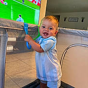 Kaiden joined the competition — help win amazing prizes! toddler, baby, child, playpen, smiling, indoor, blue_clothing, shorts, handle, television, soccer, sports, floor, wall, home, person, happy, standing, face, room