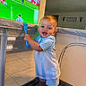 toddler, baby, child, playpen, smiling, indoor, blue_clothing, shorts, handle, television, soccer, sports, floor, wall, home, person, happy, standing, face, room