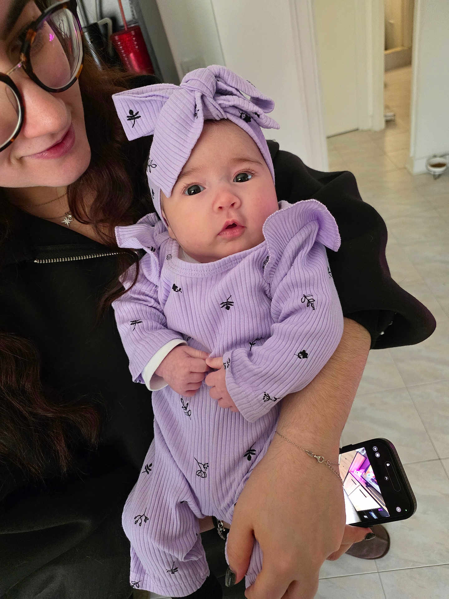 Maddy participe au concours pour gagner de l'argent avec cette photo : baby, woman, glasses, headband, lilac, outfit, holding, phone, indoor, floor, tile, hand, portrait, face, expression, long_hair, jewelry, bracelet, black_clothing, curly_hair
