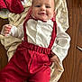 baby, child, smile, face, white_shirt, red_pants, red_suspender, bow_tie, blanket, wooden_table, clothing, person, cute, indoors, happy, infant, portrait, baby_garment, baby_fashion, table