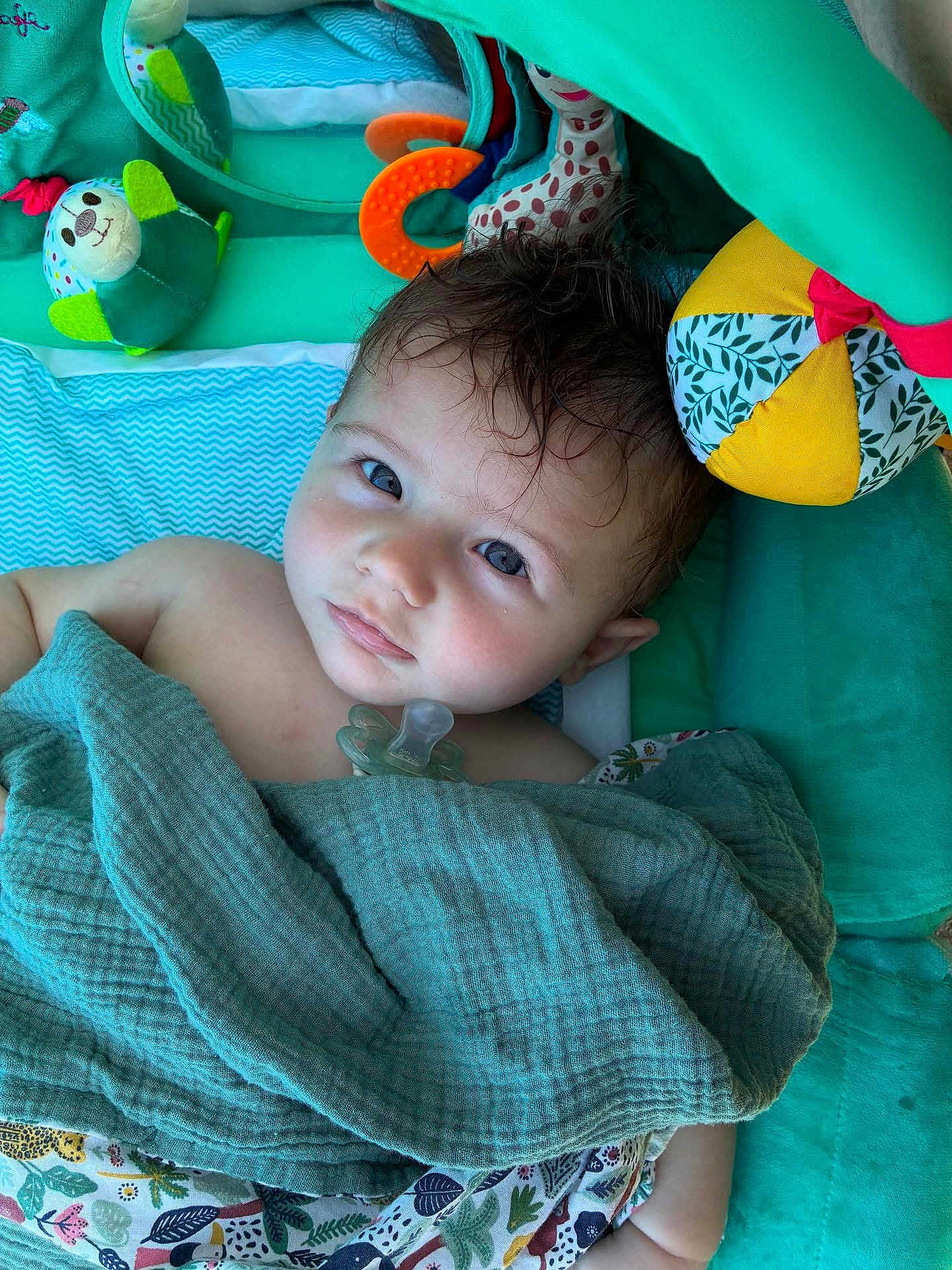 Jules participe au concours pour gagner de l'argent avec cette photo : baby, blanket, pacifier, toy, mirror, play_mat, plush_toy, colorful, infant, child, cute, face, expression, soft_texture, fabric, indoor, portrait, looking_up, wrapped, comfort
