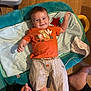 Jules a rejoint le concours — aidez-le/la à gagner de superbes lots ! baby, child, infant, orange_shirt, striped_shorts, play_mat, wooden_floor, smiling, happy, hand, foot, person, indoor, cute, waving, clothing, textile, toy, parent, family