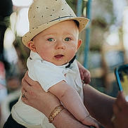 Eliott a rejoint le concours — aidez-le/la à gagner de superbes lots ! adult_hand, baby, blue_eyes, blurred_background, bracelet, casual, child, closeup, cute, expression, face, fashion, hat, holding, infant, outdoor, person, portrait, skin, white_shirt