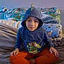 Kyo G participe au concours pour gagner de l'argent avec cette photo : bed, blanket, boy, calm_expression, cartoon_pillow, casual_clothing, child, cozy, cross_legged, frog_graphic, hoodie, indoor, leafy_pattern, orange_pants, pillow, portrait, relaxed, sitting, soft_lighting, young