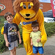 Kyo G a rejoint le concours — aidez-le/la à gagner de superbes lots ! building, child, children, clouds, daytime, event, fun, greenery, happy, lion_costume, mascot, outdoor, person, posing, shorts, sky, smile, sneakers, tshirt, yellow_costume