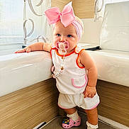 Ella participe au concours pour gagner de l'argent avec cette photo : toddler, child, baby, pacifier, pink_bow, headband, indoor, bathroom, bathtub, white_clothing, pink_shoes, crocs, socks, wood_paneling, curtains, window, standing, cute, fashion, accessories
