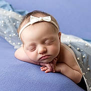 Lorelai is registered to the contest to win money with this photo: baby, sleeping, headband, bow, blue_background, pearl_decor, soft_fabric, newborn, portrait, peaceful, infant, closeup, resting, cute, hands_together, skin, face, peaceful_expression, toddler, indoors