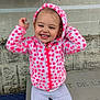 child, toddler, hoodie, pink, polka_dot, smiling, bench, outdoor, casual_clothing, sneakers, happy, face, urban, bus_stop, concrete_wall, poster, seated, cute, playful, jacket
