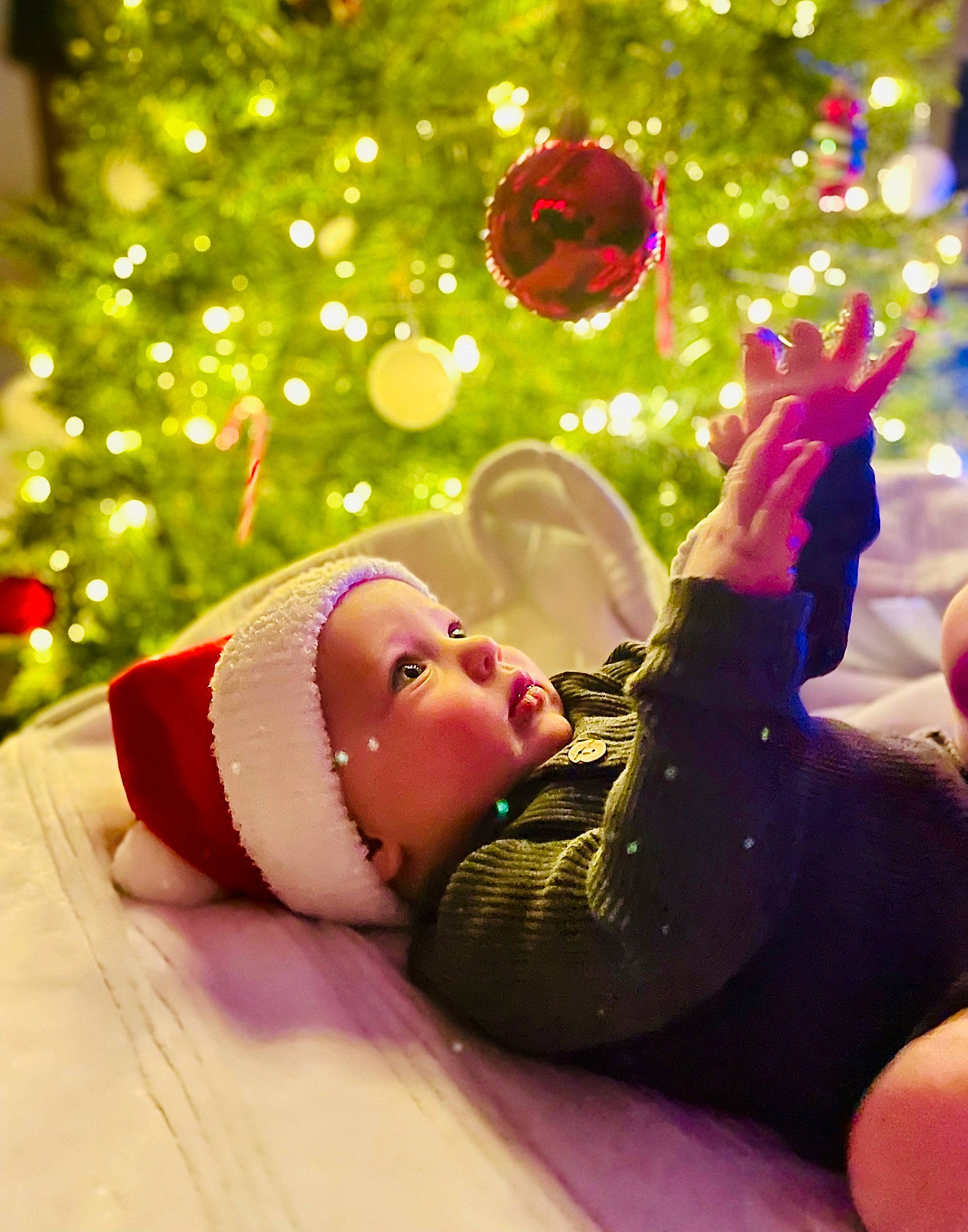 Trace is registered to the contest to win money with this photo: baby, child, christmas, christmas_decoration, christmas_lights, christmas_ornament, christmas_tree, event, foot, fun, gesture, happy, headwear, holiday, holiday_ornament, human_body, nail, ornament, people_in_nature, person