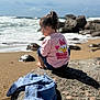 child, beach, rock, ocean, waves, sky, clouds, denim_jacket, pink_shirt, daisy_duck, pony_tail, sand, casual_clothing, seaside, nature, outdoor, relaxed, sunlight, shadow, person