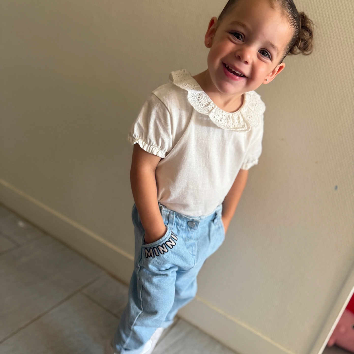 Svetlana participe au concours pour gagner de l'argent avec cette photo : blue_jeans, casual_clothing, child, cute, fashion, floor_tiles, girl, hair_buns, hands_in_pockets, happy, indoor, playful, portrait, smiling, standing, toddler, wall, white_shirt, white_shoes, young_child