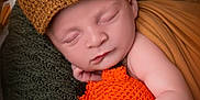 Ismaël participe au concours pour gagner de l'argent avec cette photo : baby, sleeping, knitted_hat, plush_toy, orange, brown, blanket, cozy, cute, infant, soft_texture, closeup, resting, peaceful, hand, face, child, portrait, indoors, warm_colors