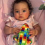 Cataleya is registered to the contest to win money with this photo: baby, infant, curly_hair, pink_blanket, knitted_toy, colorful, crocodile_toy, clothing, cute, portrait, child, soft_lighting, indoors, hand, playful, lying_down, close_up, expression, fabric, adorable