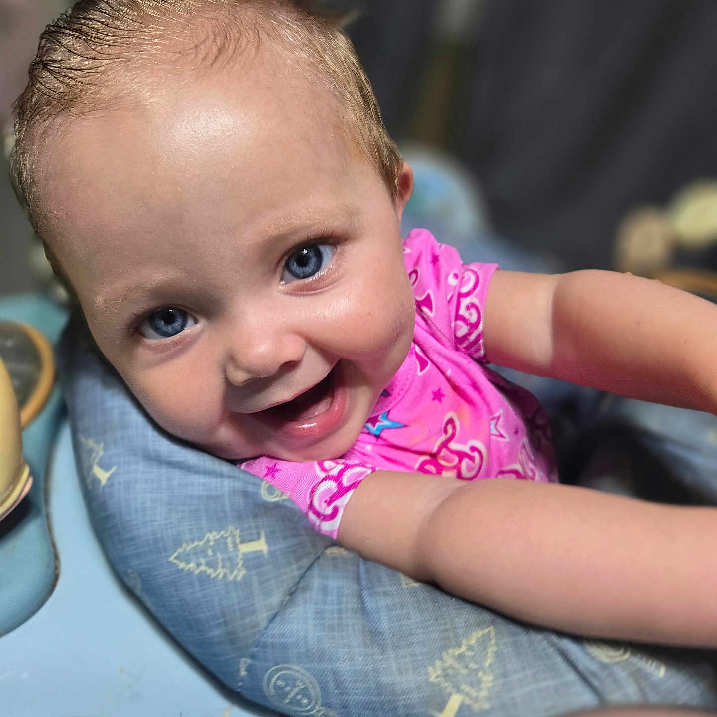 Rylee is registered to the contest to win money with this photo: arm, baby, baby_seat, blue_eyes, child, close_up, cute, expression, face, happy, indoor, infant, pattern, person, pink_shirt, portrait, skin, smiling, tree_pattern, young_child