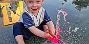 Hudson joined the competition — help win amazing prizes! toddler, child, water_fountain, water, playing, outdoor, park, wet_hair, smiling, happy, blue_eyes, sitting, pavement, reflection, people, trees, daylight, clothing, barefoot, fountain_lights