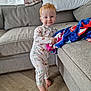 Hudson is registered to the contest to win money with this photo: toddler, child, red_hair, standing, blanket, couch, living_room, smile, pajamas, curtains, window, floor, footwear_bare, home_interior, furniture, person, cute, happy, indoors, playful