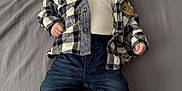 John is registered to the contest to win money with this photo: baby, infant, pacifier, plaid_shirt, white_top, jeans, sneakers, bed, gray_bedspread, lying_down, clothing, footwear, cute, child, person, indoors, young, fashion, casual, portrait