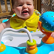 Phoenix joined the competition — help win amazing prizes! baby, child, smiling, yellow_clothing, baby_walker, toy, outdoor, wooden_deck, happy, face, infant, sunlight, playful, colorful, person, young_child, cute, cheerful, seat, daylight
