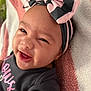 baby, black, bow, child, closeup, clothing, cute, expression, face, happy, headband, infant, lying_down, person, pink, portrait, skin, smiling, towel, young