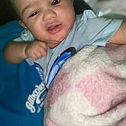 Kaiairi is registered to the contest to win money with this photo: baby, child, blanket, blue_shirt, closeup, face, expression, indoor, infant, person, portrait, skin, soft_texture, young, lying_down, curious, puzzled, comfort, warm, casual_clothing