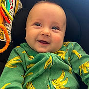 Odie joined the competition — help win amazing prizes! baby, infant, child, car_seat, smiling, green_hoodie, banana_pattern, toy, orange_toy, brand_logo, warning_label, close_up, portrait, cheeks, bright_eyes, seat, fabric, happy, cute, soft_light