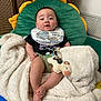 baby, infant, child, blanket, toy, stuffed_animal, cushion, bib, smiling, indoor, floor_mat, colorful, cute, happy, clothing, person, foot, hand, head, face