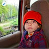 child, toddler, car_seat, red_beanie, necklace, jacket, plaid, window, car_interior, seat, serious_expression, portrait, young_child, face, person, outdoor_background, nature, casual, travel, autumn_wear