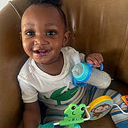 Carson is registered to the contest to win money with this photo: toddler, baby, child, smiling, happy, bottle, toy, frog, monkey, striped_pants, white_shirt, crocodile_print, chair, indoor, cute, playful, person, sitting, face, portrait