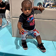 Major is registered to the contest to win money with this photo: toddler, child, boy, indoor, clothing, shorts, tshirt, sneakers, spiderman, chain, cushion, bench, people, background, reflection, play_area, portrait, person, floor, hand