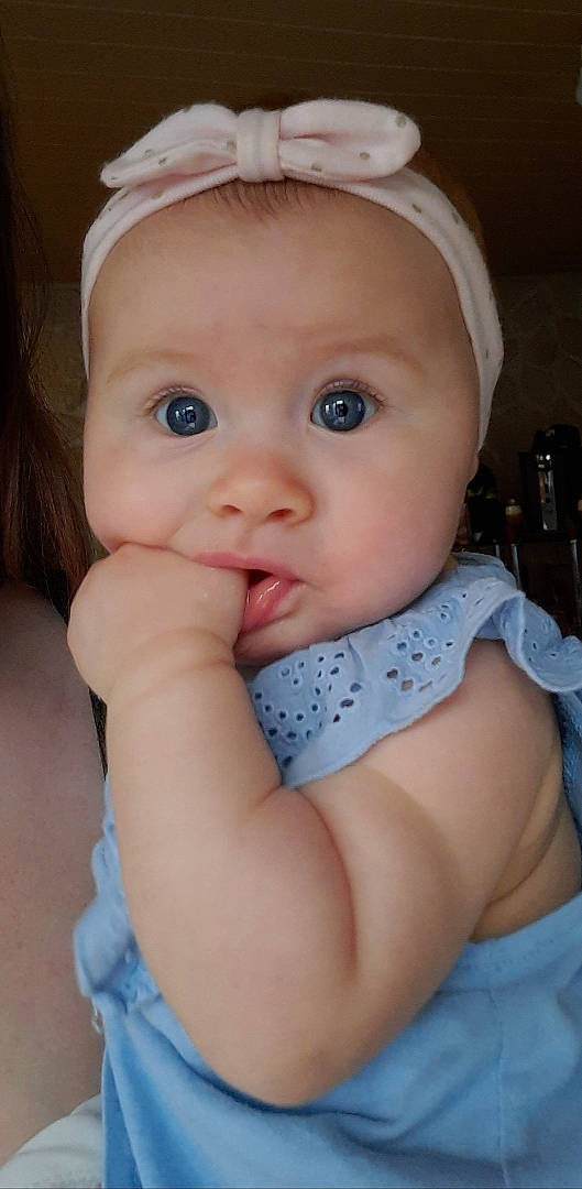 Kélia participe au concours pour gagner de l'argent avec cette photo : baby, baby_toddler_clothing, blue, cheek, chin, dress, eyebrow, eyelash, facial_expression, hair, head, headgear, iris, lip, mouth, neck, nose, person, pink, skin