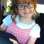 Kayla joined the competition — help win amazing prizes! child, girl, glasses, smile, car, seat, pink_dress, white_shirt, hair, hand, portrait, happy, indoors, vehicle, young, casual_clothing, person, childhood, cute, playful