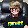 child, boy, smile, glasses, tshirt, fortnite, black_clothing, leather_chair, indoor, portrait, happy, casual, seated, young, person, hair, head, face, comfortable, relaxed