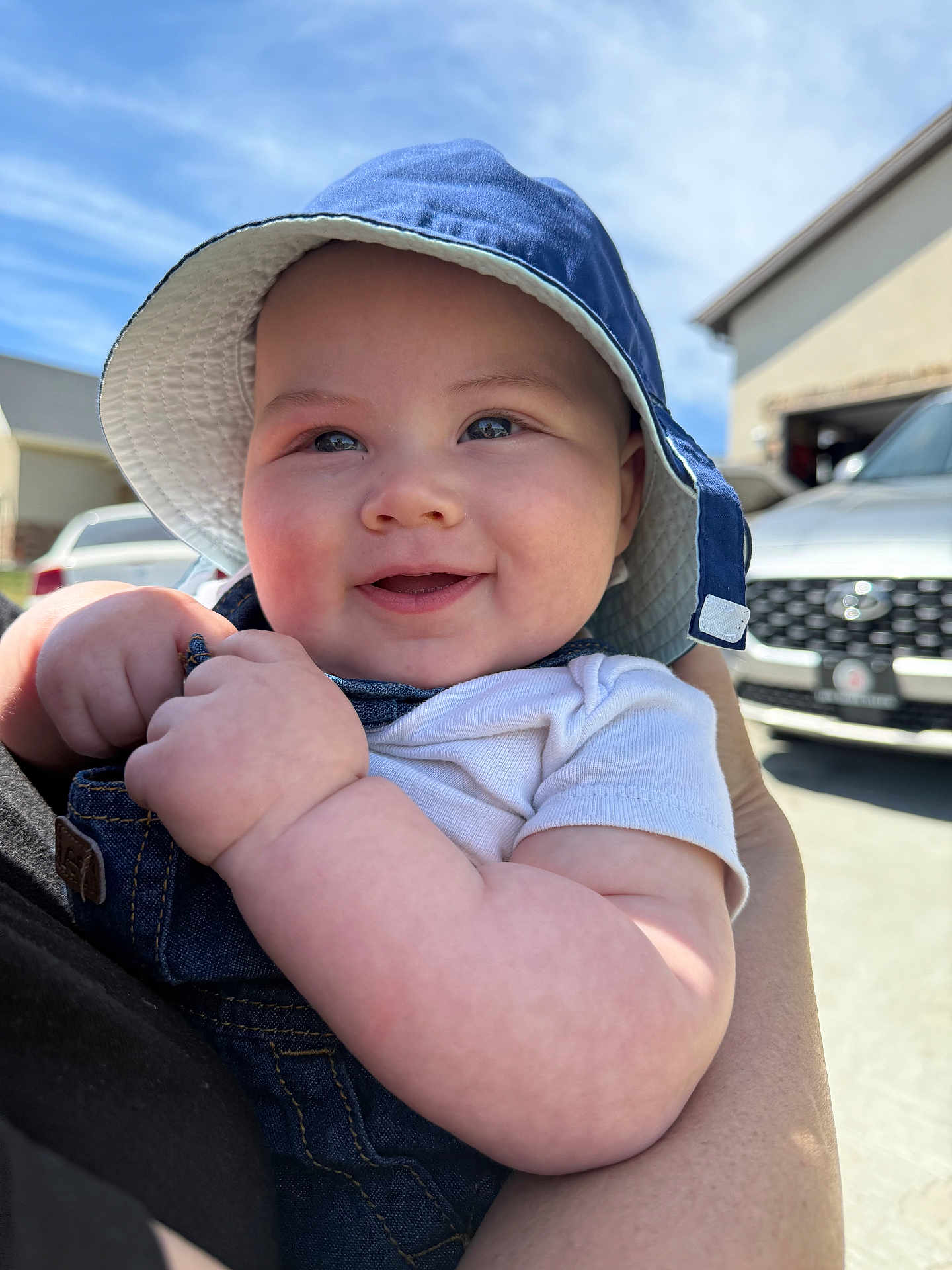 Marcelo joined the competition — help win amazing prizes! baby, child, smiling, hat, denim, overalls, outdoor, sunny, blue_sky, person, cute, holding, face, cheeks, arm, clothing, daylight, background, vehicle, house